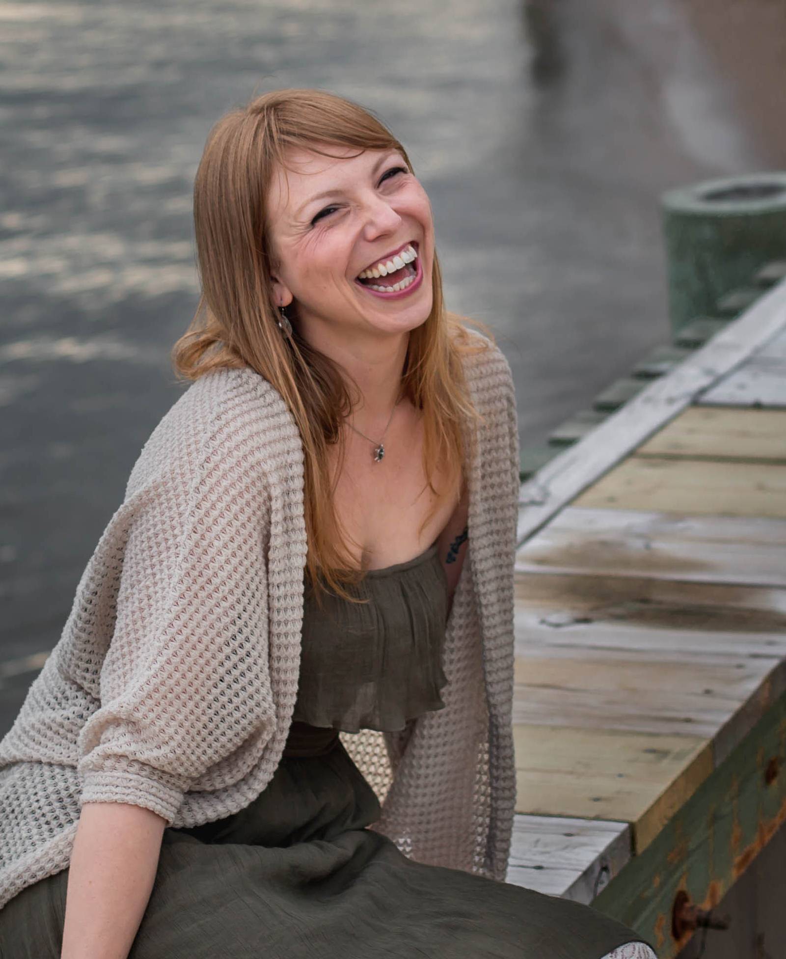 June Gervais is sitting on a wooden structure over the water and laughing. 