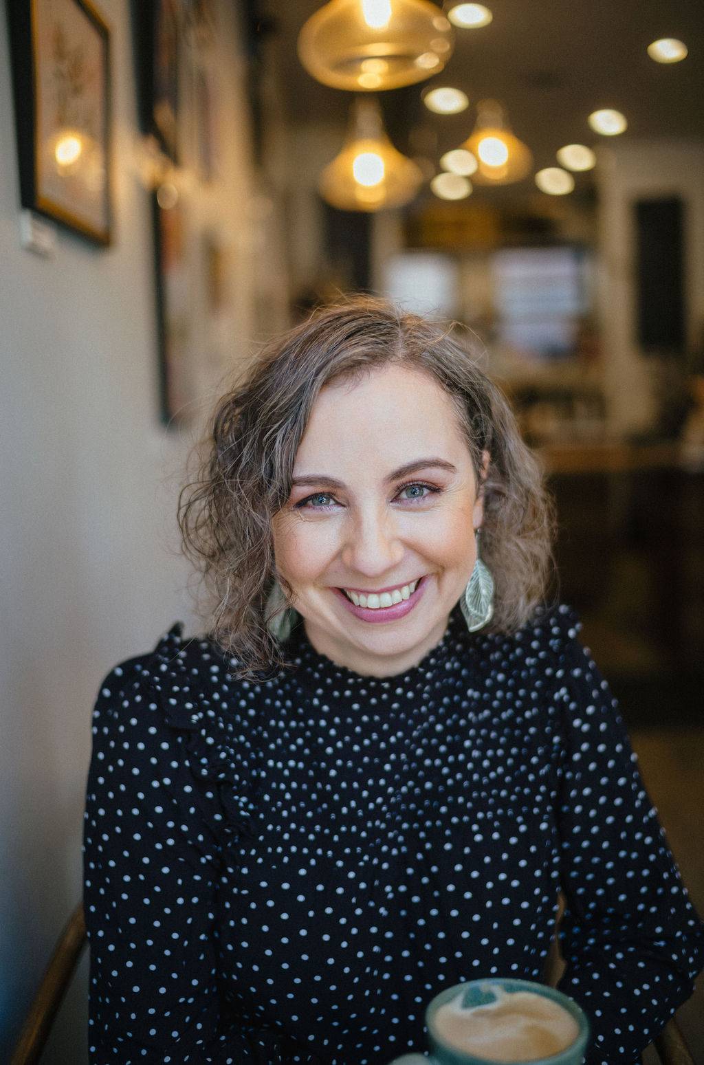 Brooke has short wavy hair and is wearing a dark shirt with white polka dots on it.