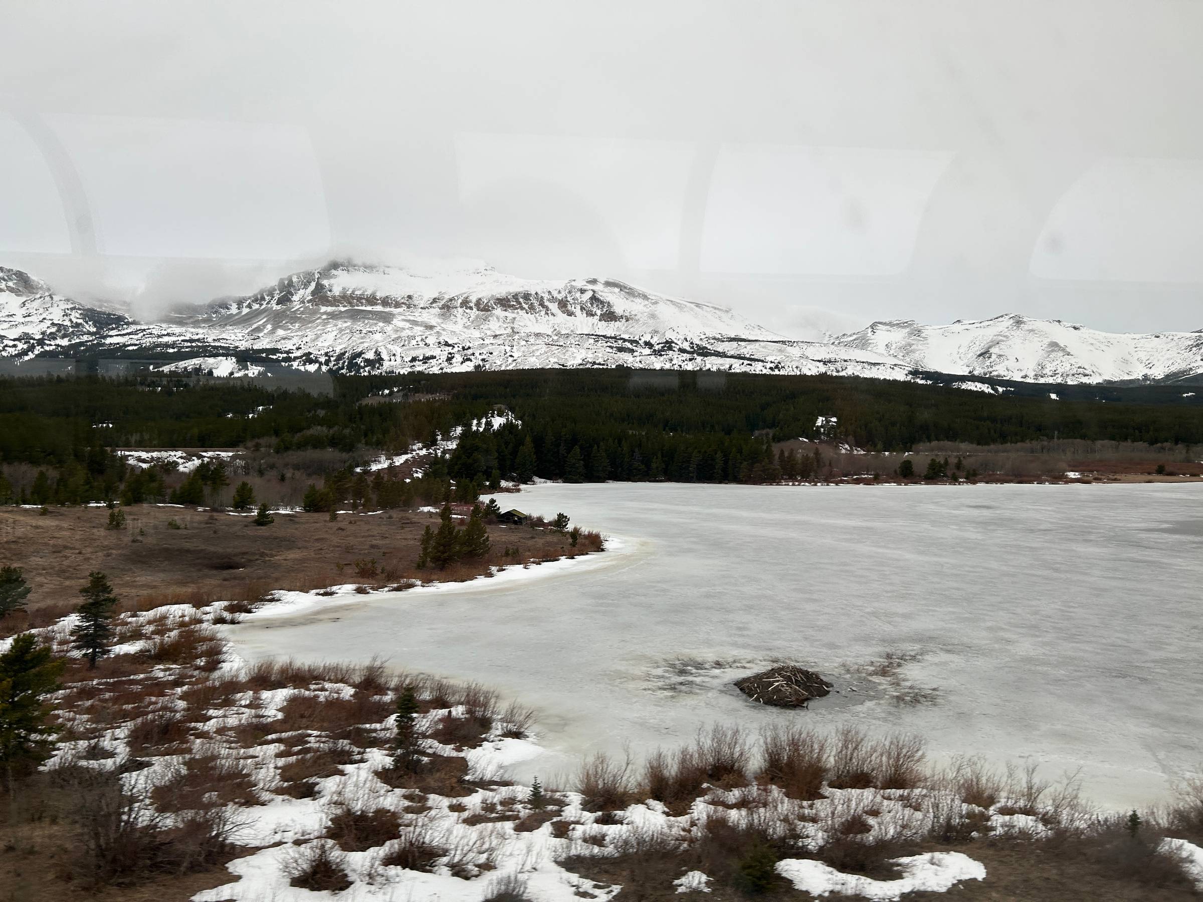 A picture taken from the viewing car of the train with mountains in the distance and a frozen lake in the foreground
