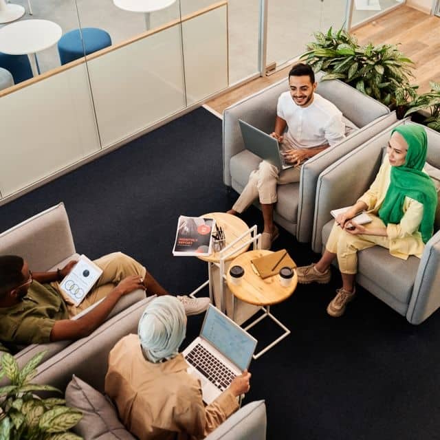 Stock photo of four people sitting in chairs, in a layout that could be in a library, and appearing to be in conversation. From https://www.pexels.com/photo/people-sitting-on-the-armchair-8069112/