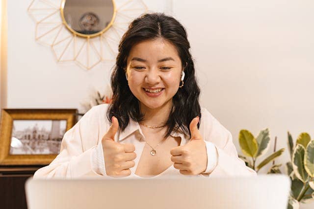 Photo of a woman looking at a laptop, smiling, and giving two thumbs up