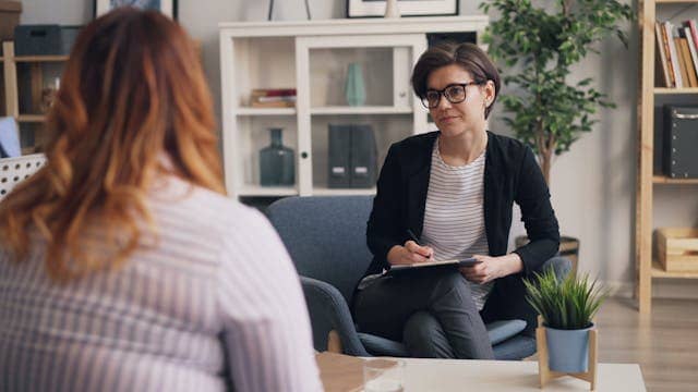A woman sitting in a chair talking to another woman