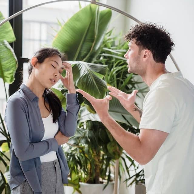 Photo of two people talking in front of potted plants. One seems angry and emphatic, while the other seems like "not this again"
