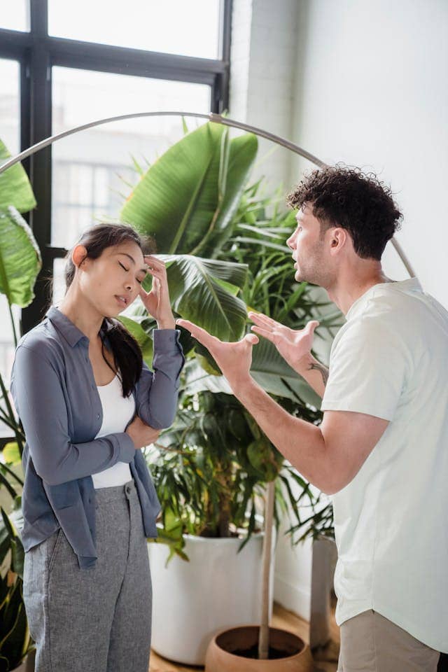 Photo of two people talking in front of potted plants. One seems angry and emphatic, while the other seems like "not this again"
