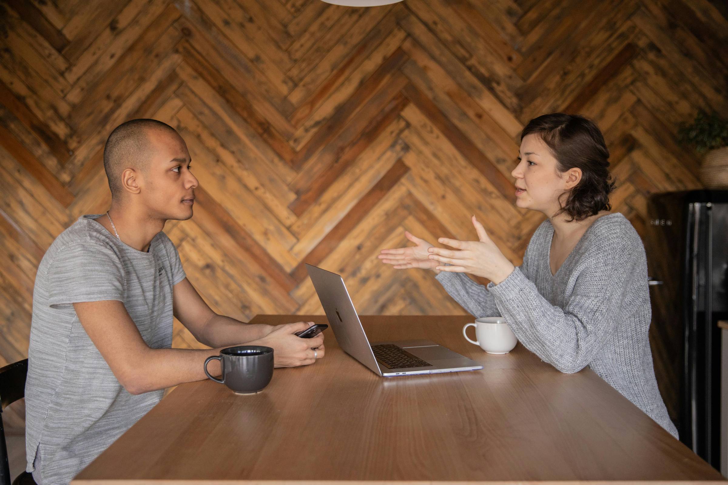 Two people sitting across an office table from one another. The female-presenting person has her hands in a position that looks like she's explaining something to the male-presenting person across from her.