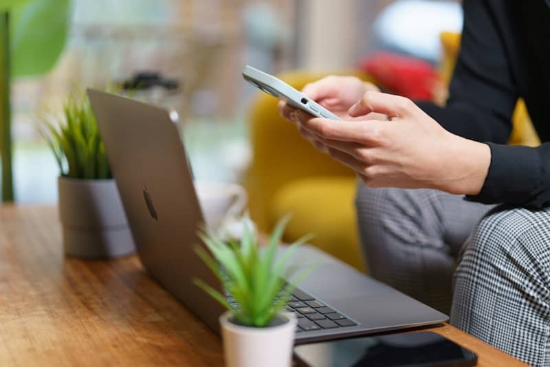 A person using a cell phone while sitting in front of a laptop