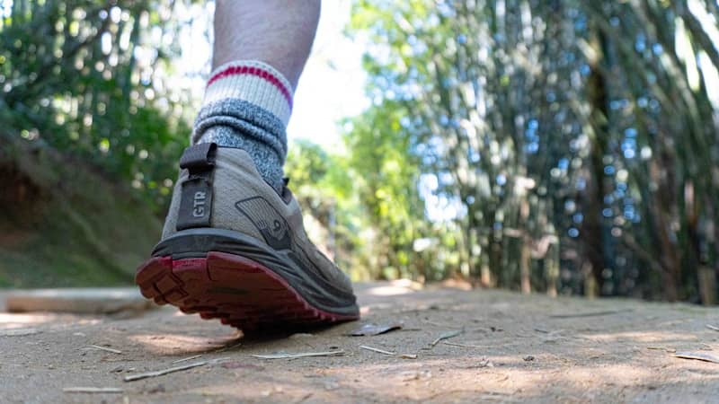 A person wearing a trail running shoe and wool socks on a dirt path