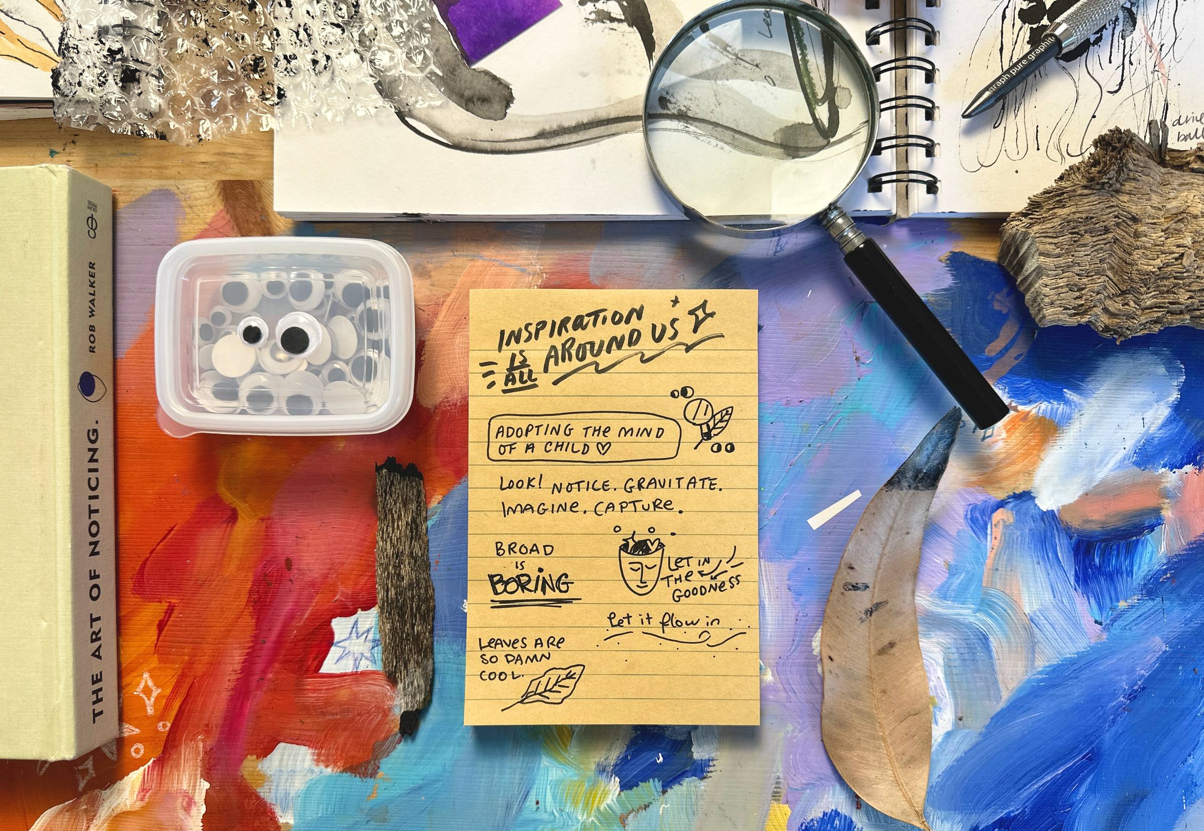 Assorted nature and art materials, googley eyes, magnifying glass, ink, and nature tools used in the art making process.