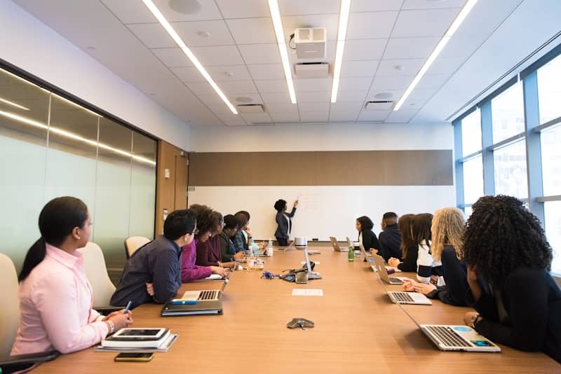 people on conference table looking at talking woman