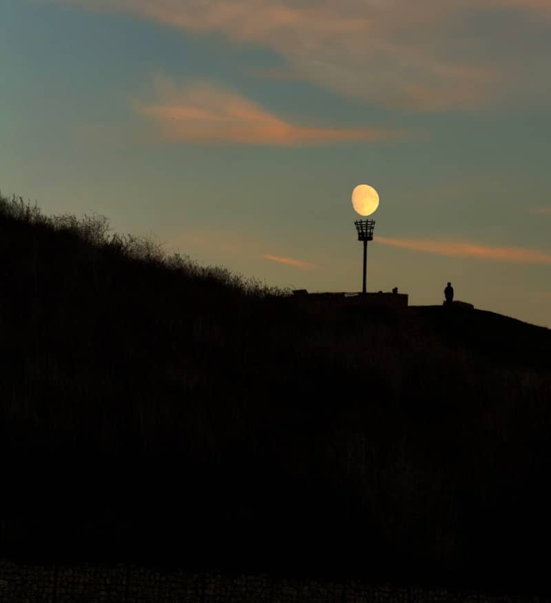 Full moon behind a tower on a hill.