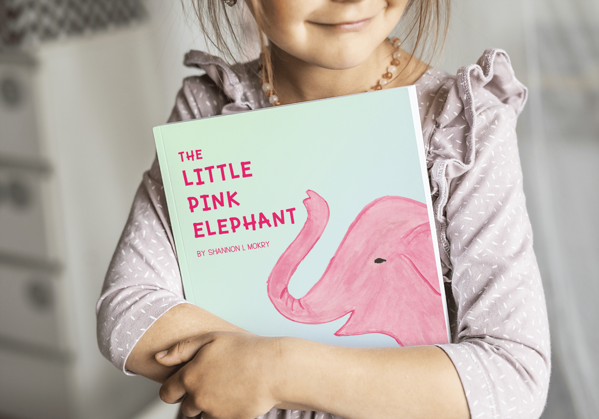 A little girl clutching a book with the title "The Little Pink Elephant' by Shannon L. Mokry. The book is a simple light green background and the head of a pink elephant