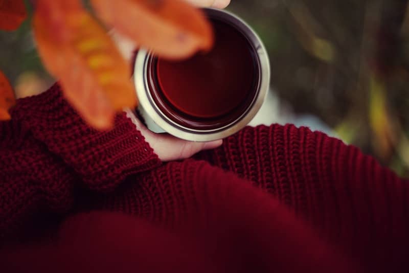 A person wearing a comfy sweater and holding a cup of tea