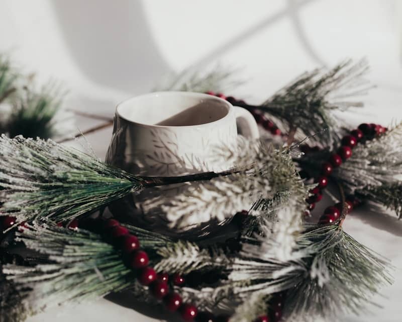 A white cup sitting on top of a table with festive winter holiday decorations