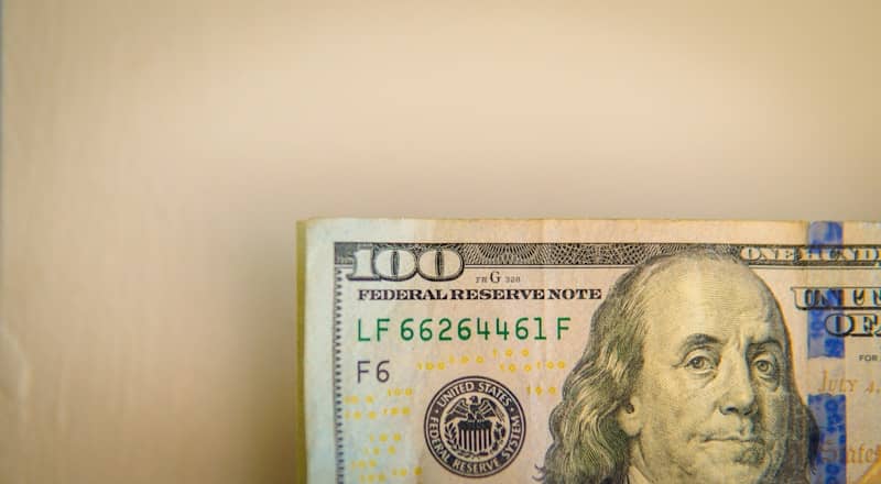A hundred dollar bill against a plain light background.