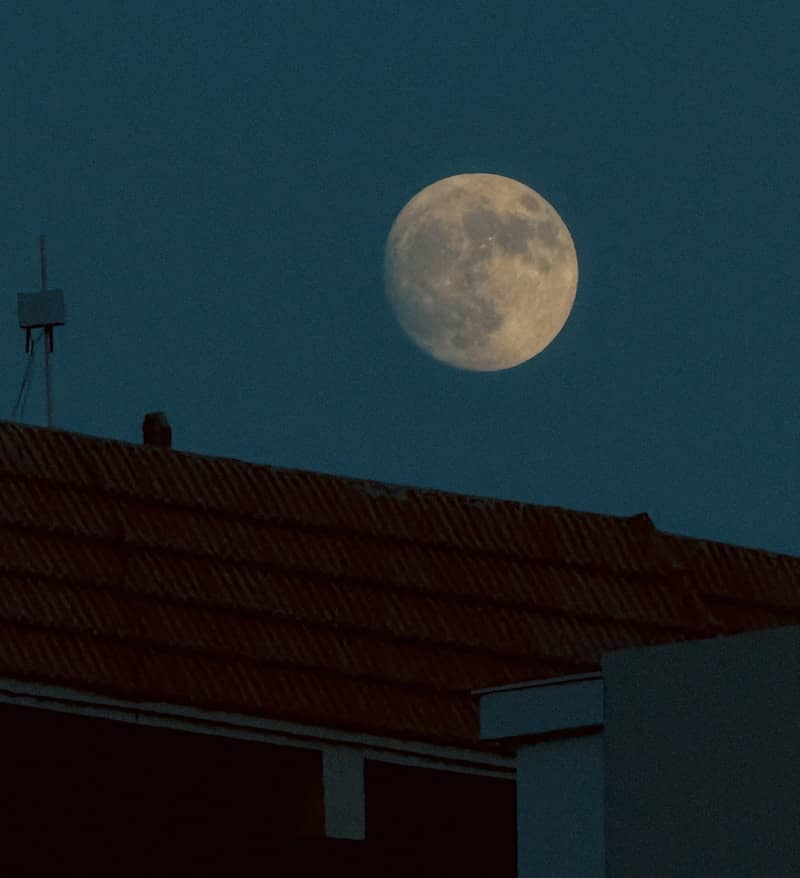 A full moon is seen over a rooftop