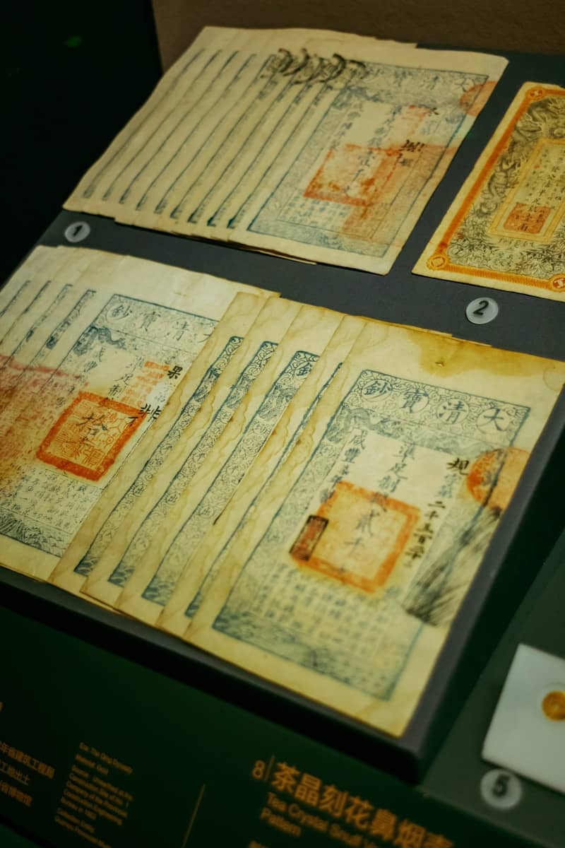 Antique paper banknotes with blue ink and red stamps displayed in a museum case.
