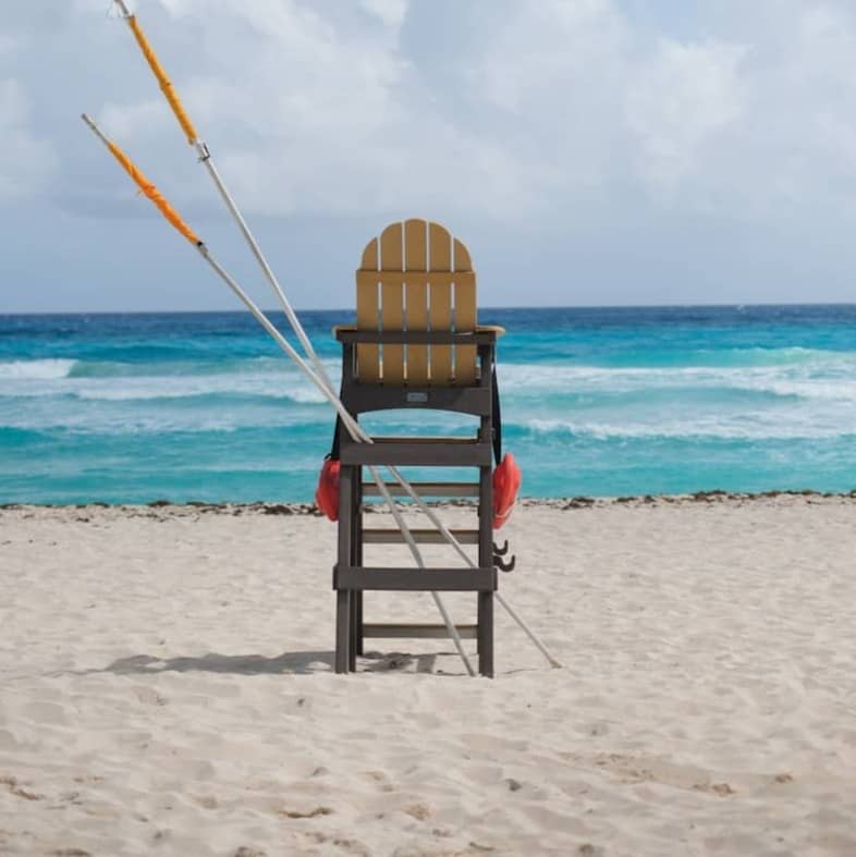 Empty lifeguard chair on a sandy beach with ocean waves.