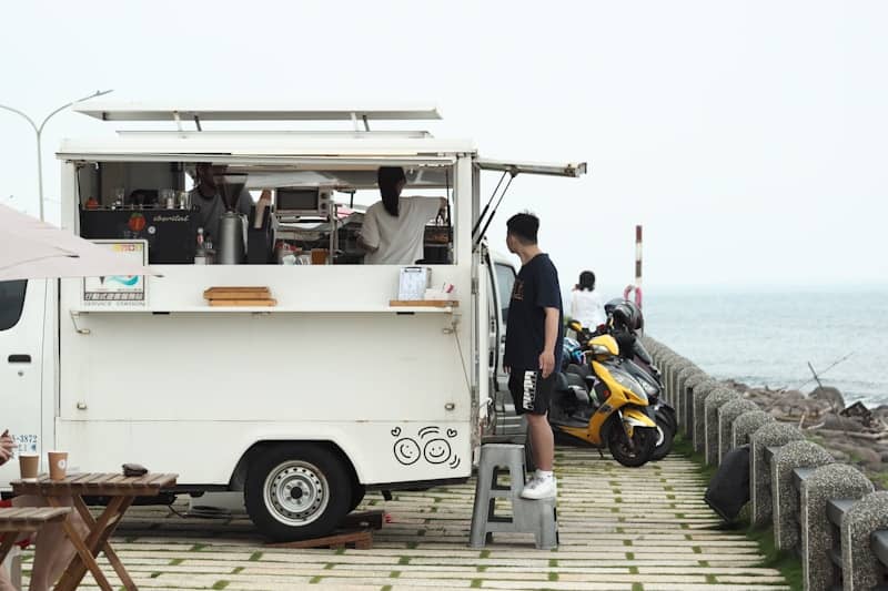 People ordering at a white food truck by the ocean.