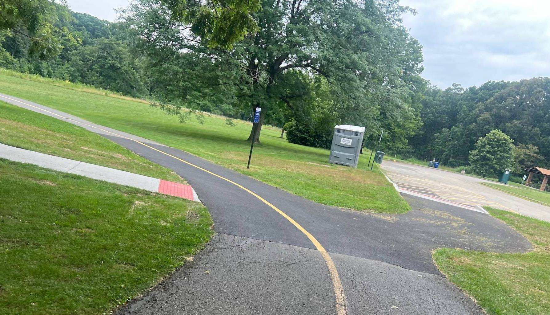 A bike trail with a new asphalt patch curves left in a forest preserve.