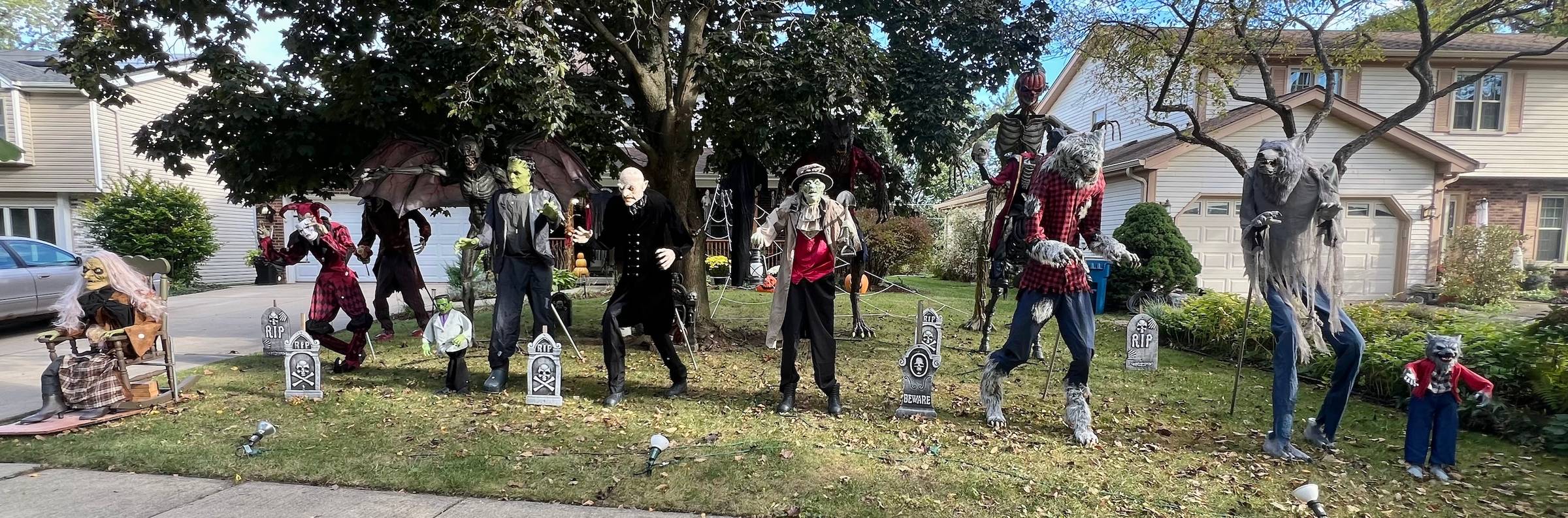 A row of tall creepy dolls lines up along a suburban lawn.