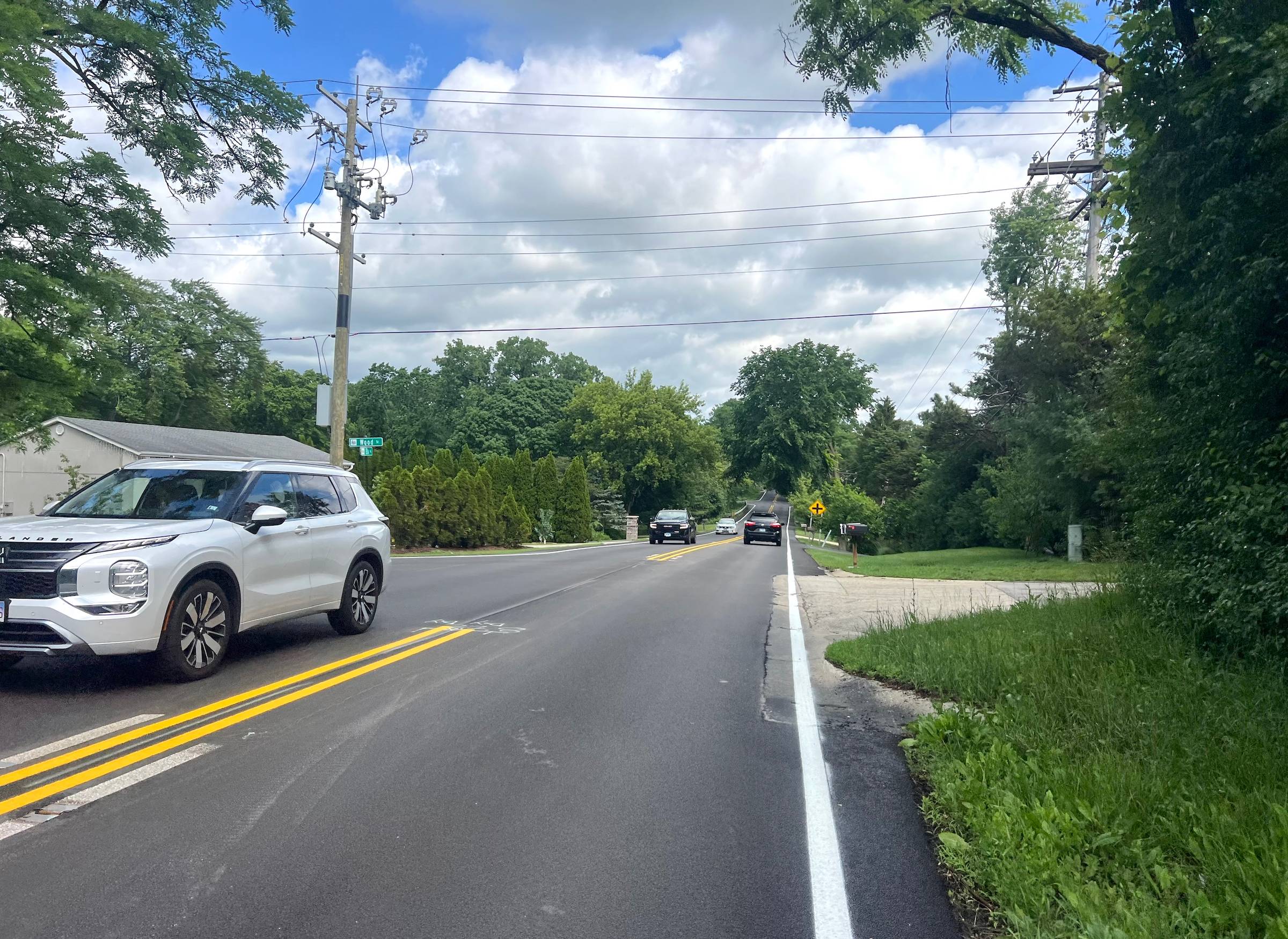 Newly paved shoulder on Ela Road in Cook County with a blue vehicle parked nearby.