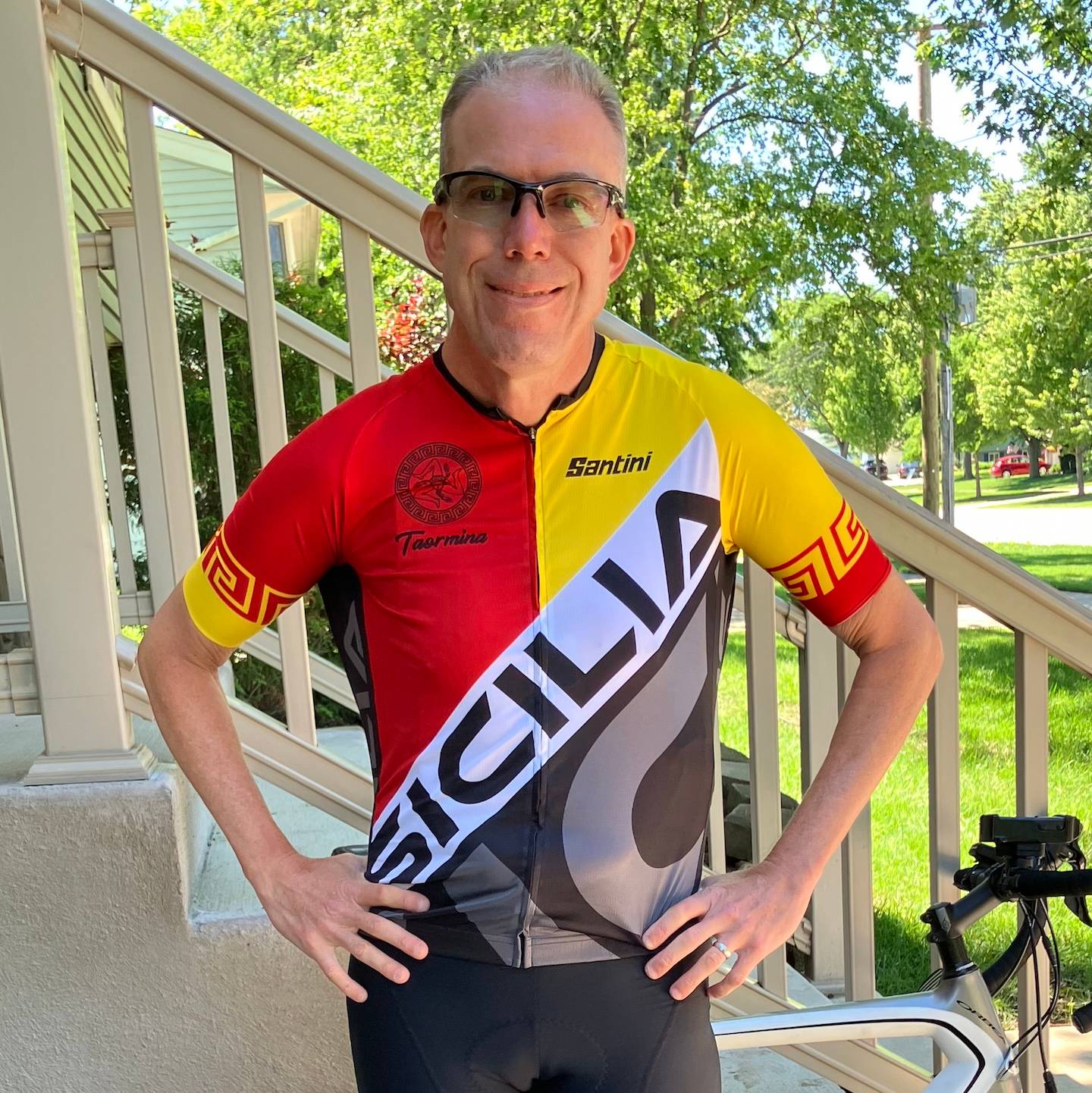 Neil poses in front of the side of front steps in a leafy neighborhood with a red, yellow and white "Sicilia" bike jersey