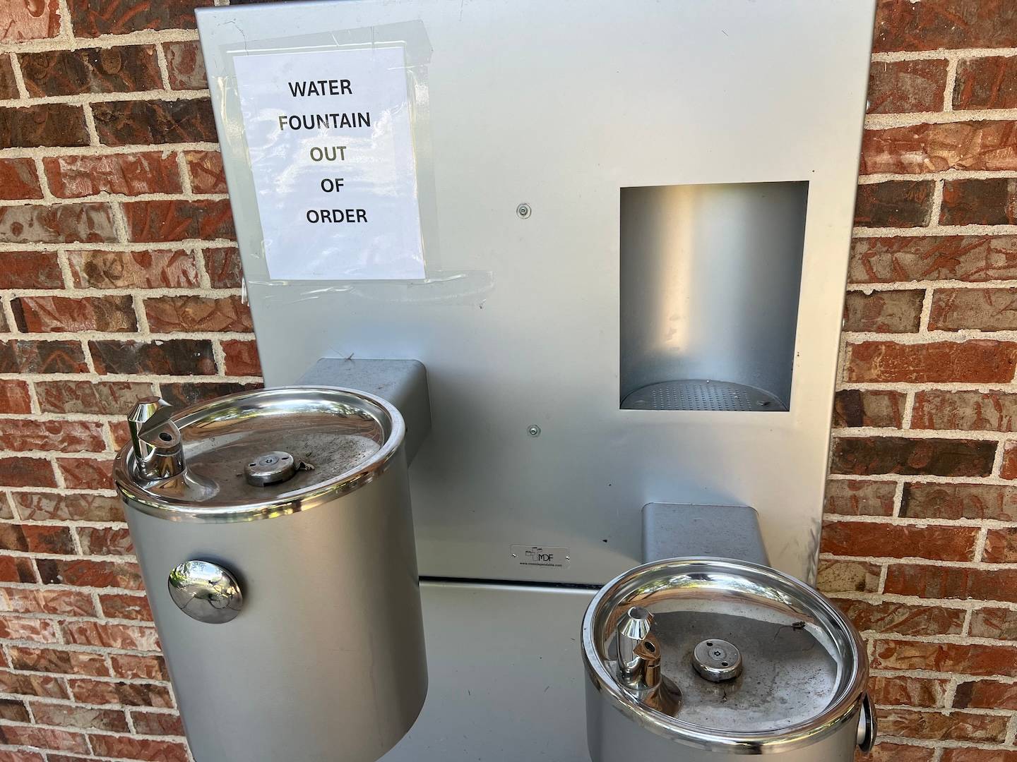 Two water fountains and a bottle-filling station appear on a brick wall, with an "out of order" sign.