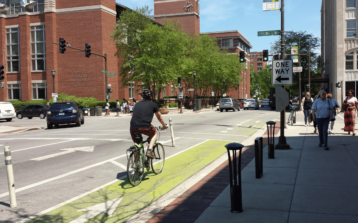 A bicyclist rides in a green-painted protected bike lane in a city downtown.