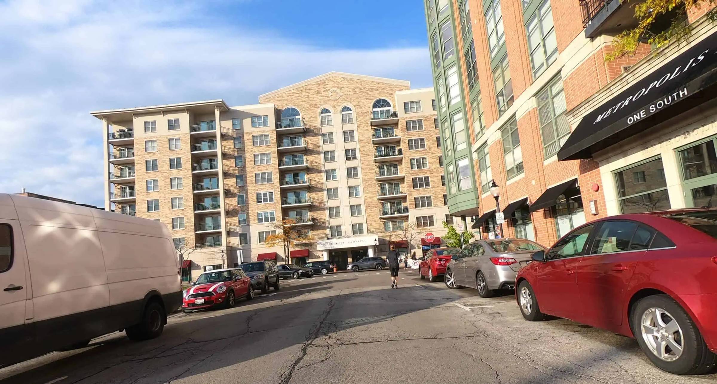 Looking down a road lined with cars and surrounded by tall new buildings in a suburban downtown
