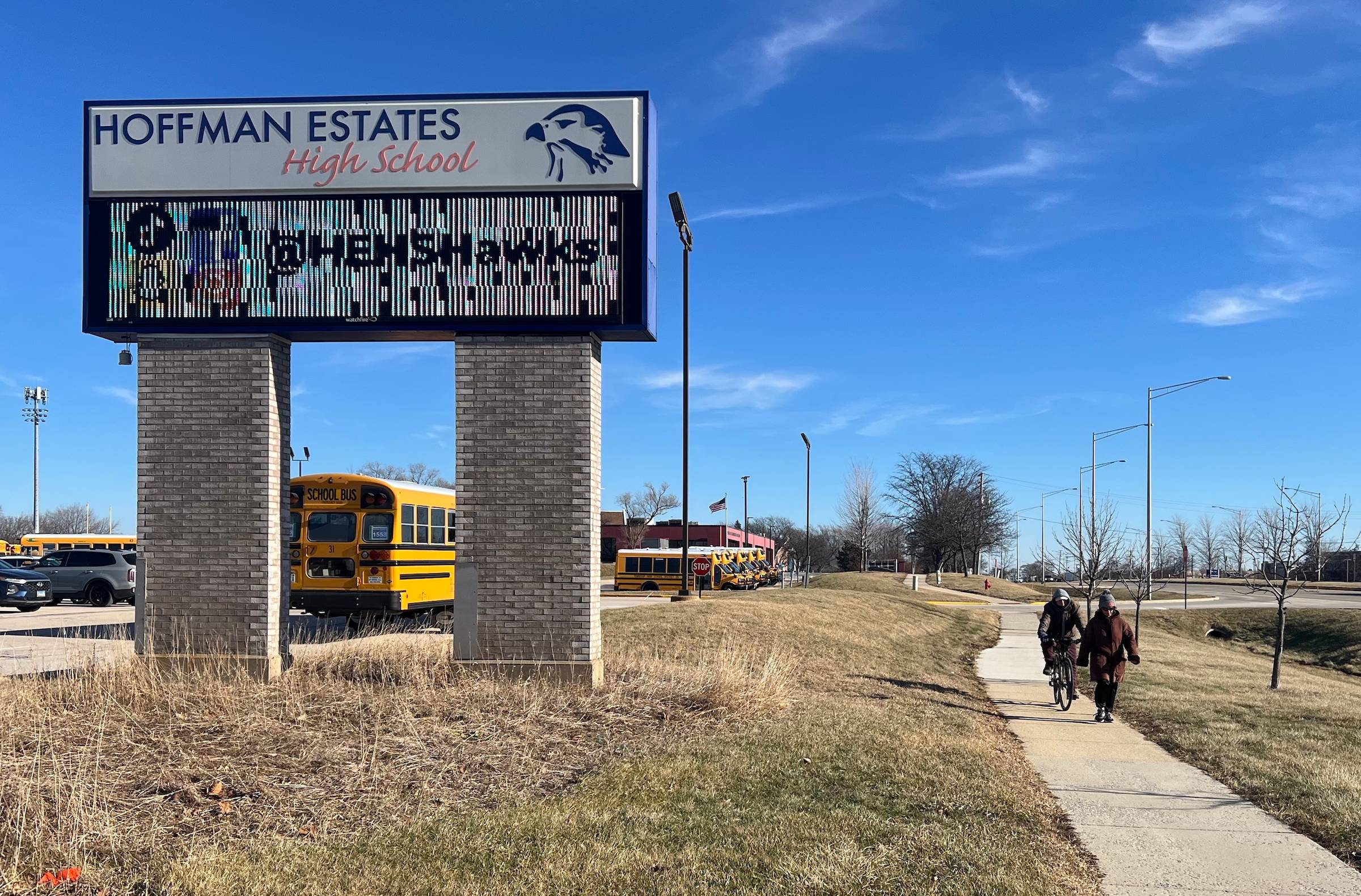 Hoffman Estates High School digital sign with text, school buses, and pedestrians biking and walking.