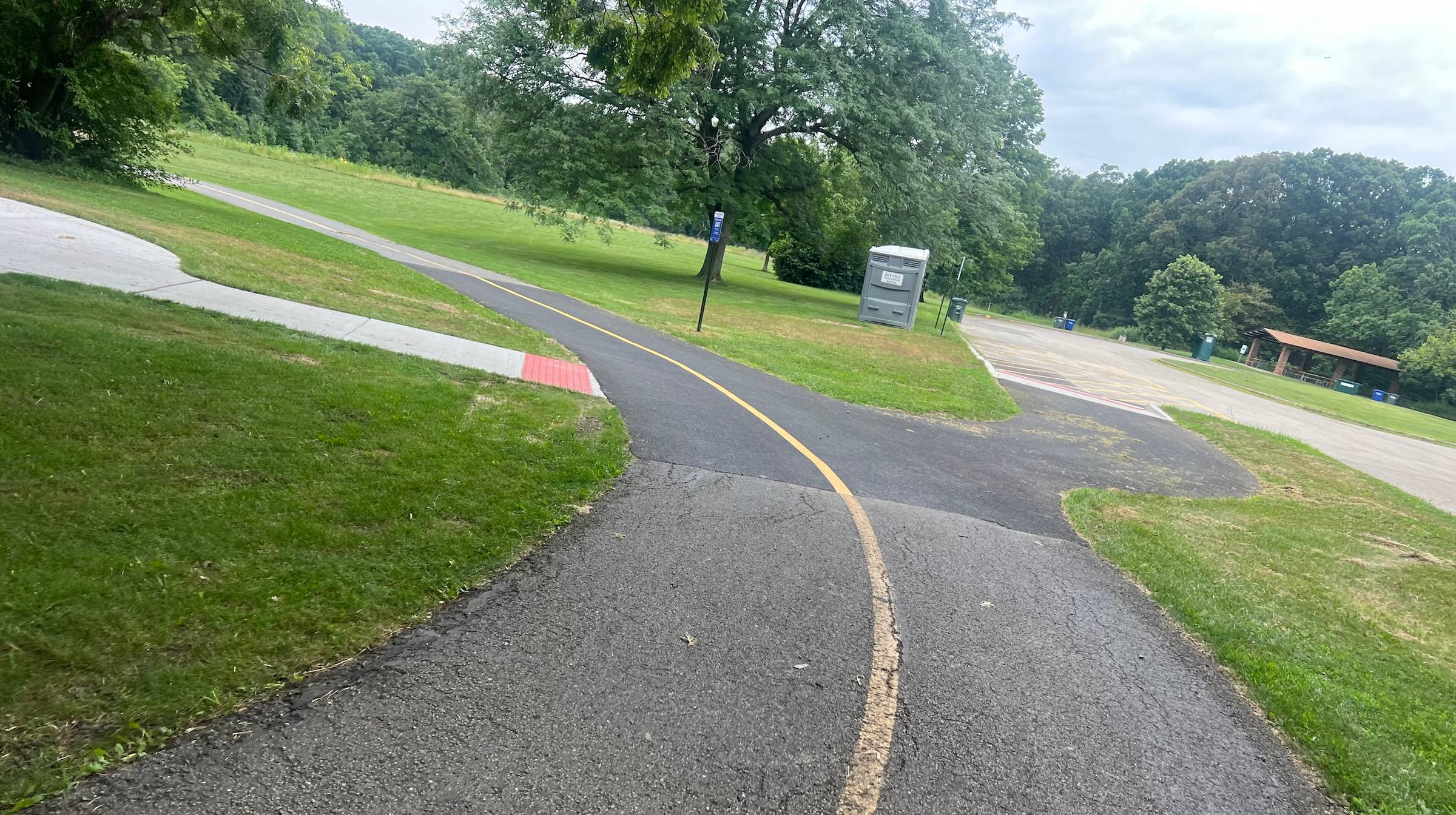 A bike trail with a new asphalt patch curves left in a forest preserve.