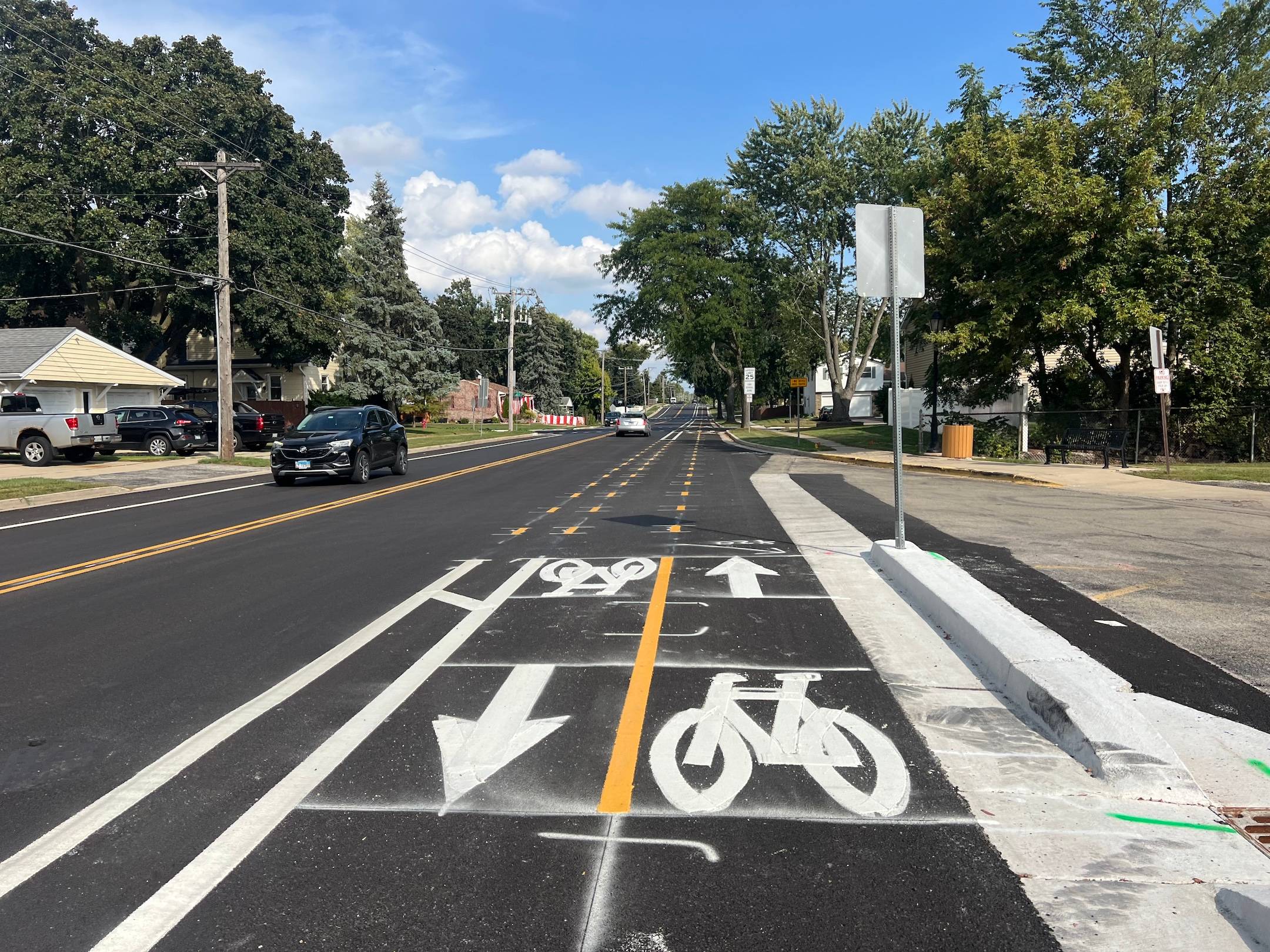 A two-way bike lane on new black asphalt appears along a suburban street.