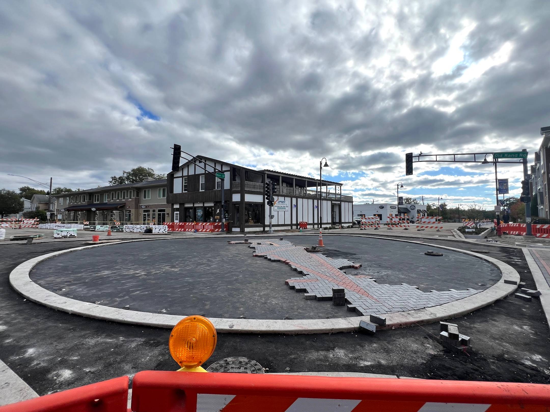 Construction barriers close off an intersection in a suburban downtown as a big circle fills the intersection, with some colored bricks starting to fill it.