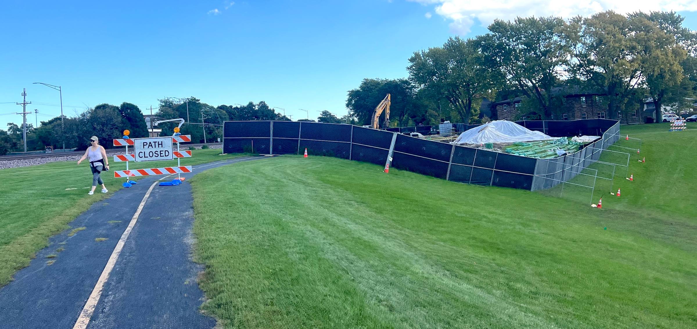 A striped trail extends to a "Path Closed" sign with a fenced off square of park land in the background, mowed grass up front