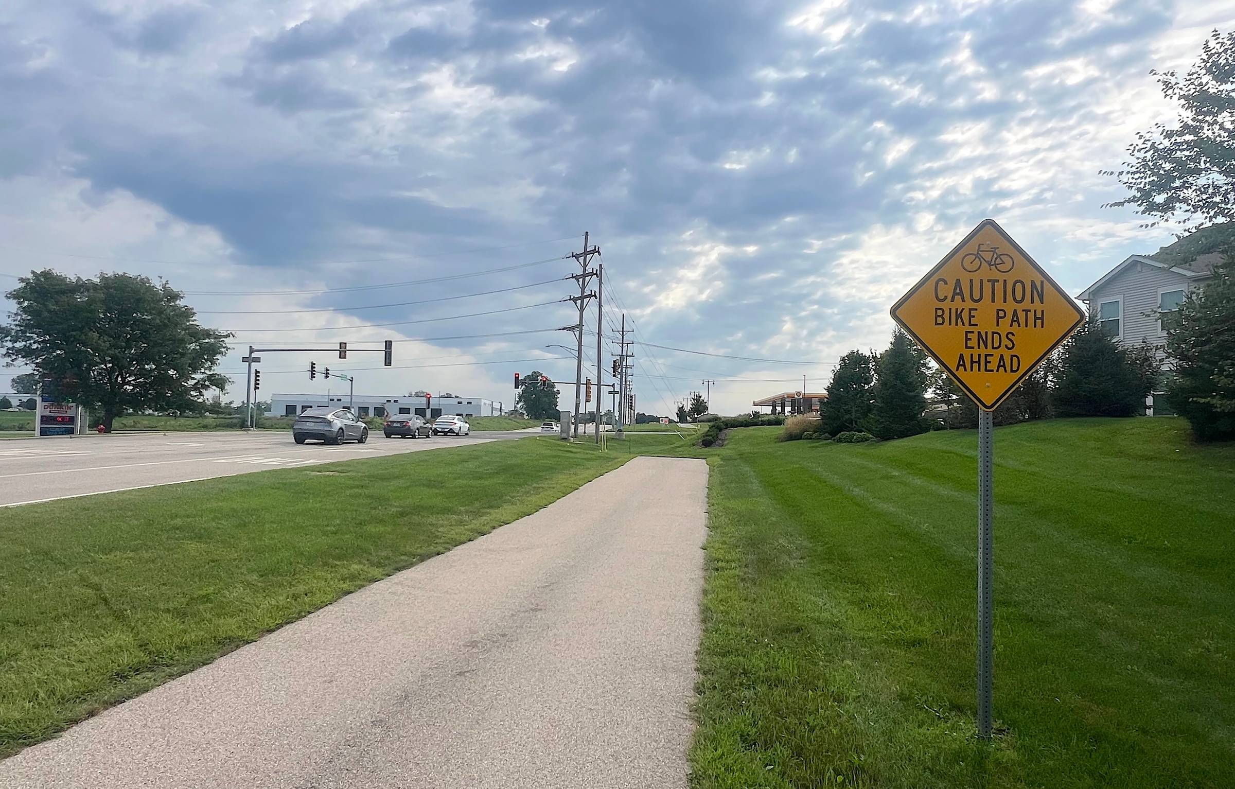 Bike path ends ahead with caution sign on grassy area near road and traffic lights.