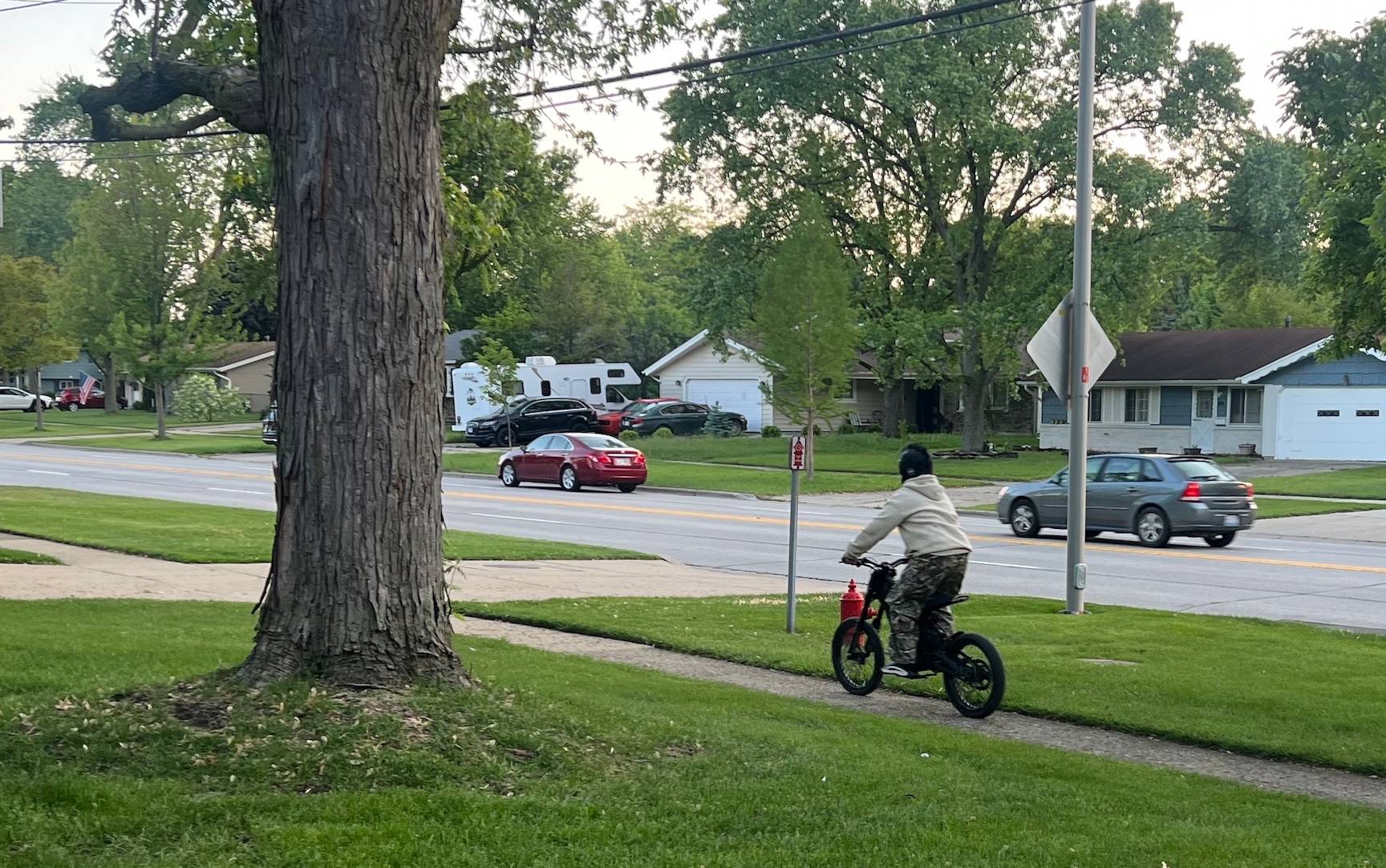 A child on a small e-bike rides on a narrow suburban neighborhood sidewalk 