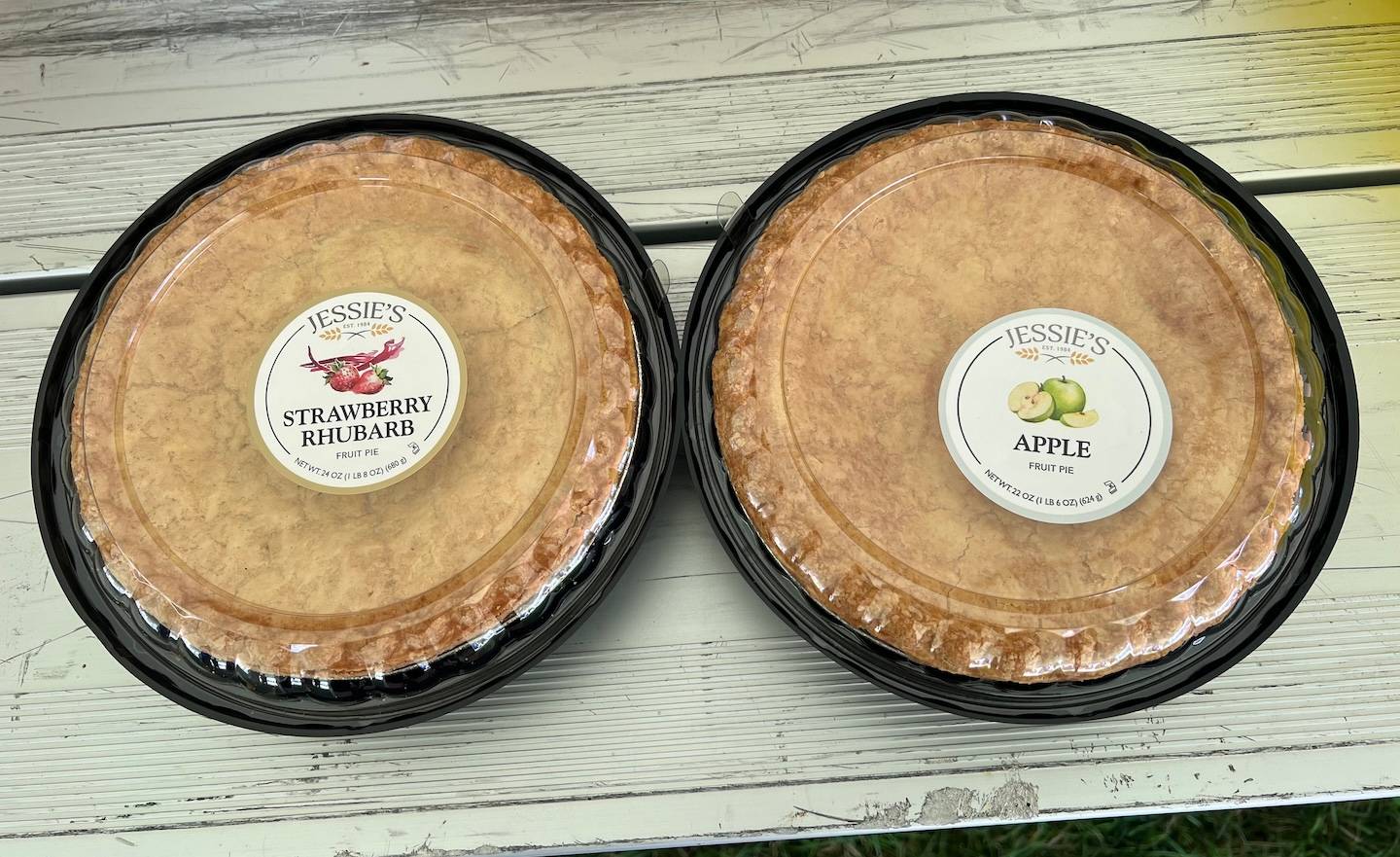A strawberry rhubarb and apple pie in plastic containers sit on a bench.