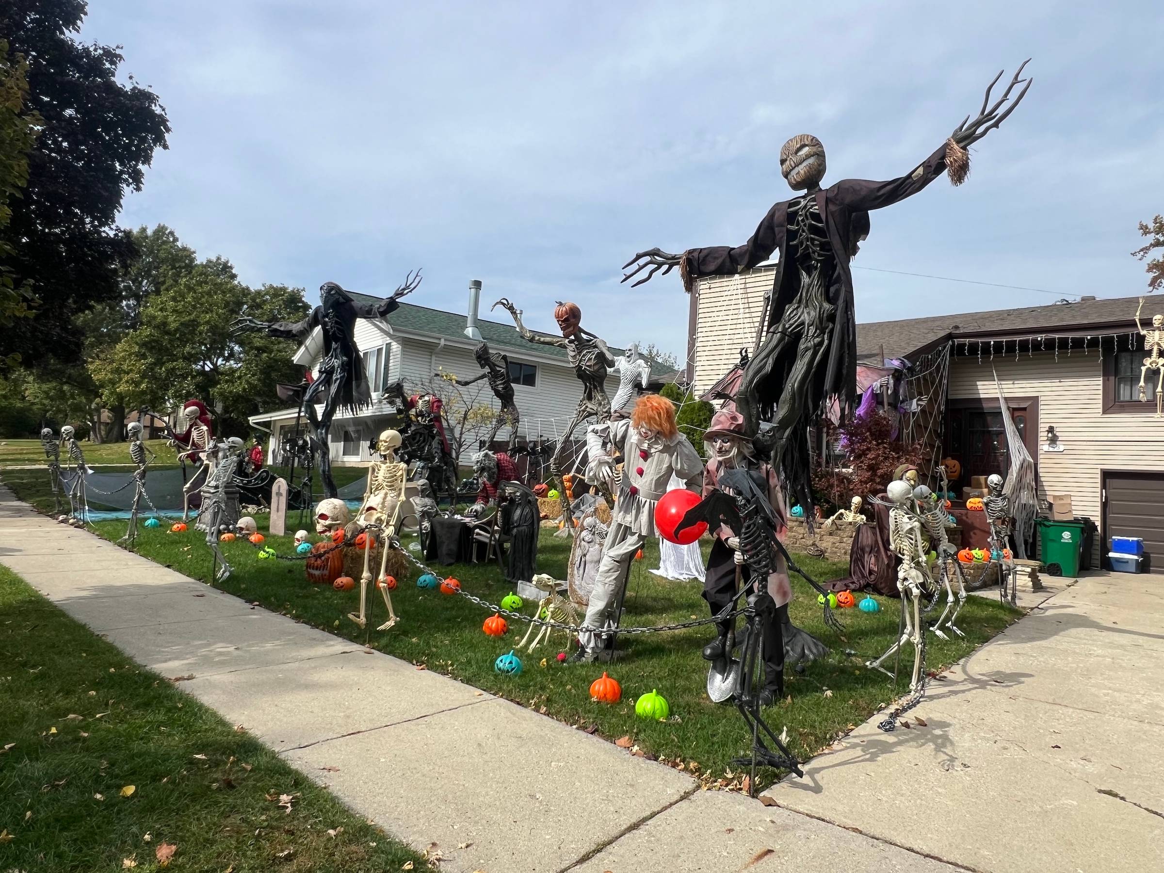 Several dolls and skeletons are flanked by tall creatures with long, branchy arms and fingers decorate a front lawn of a suburban home.