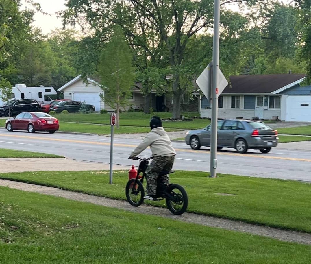 A child rides an e-moto on a suburban sidewalk.