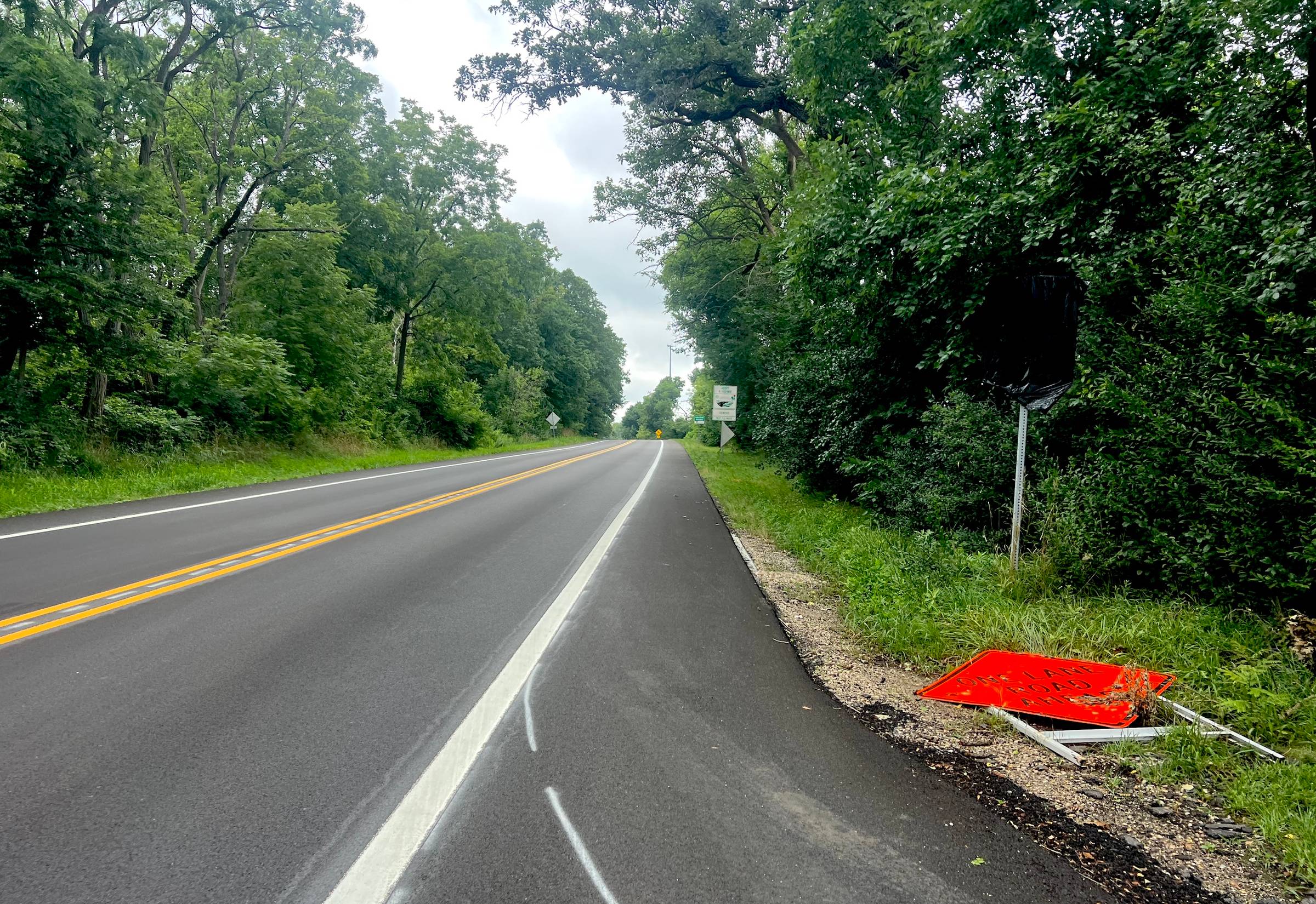 Empty rural road with trees and a construction sign on the side.