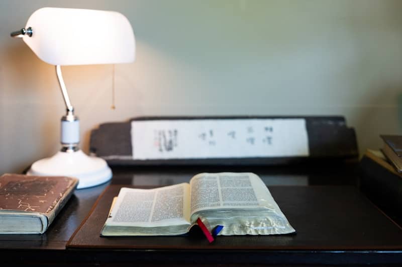 An open book rests on a desk with a lamp.