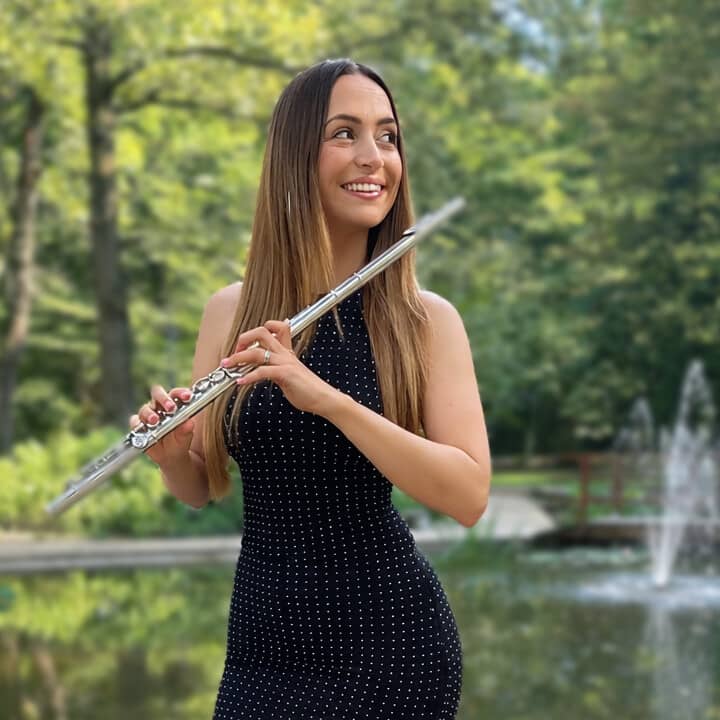 Ariana smiling and holding her flute by a pond in the park