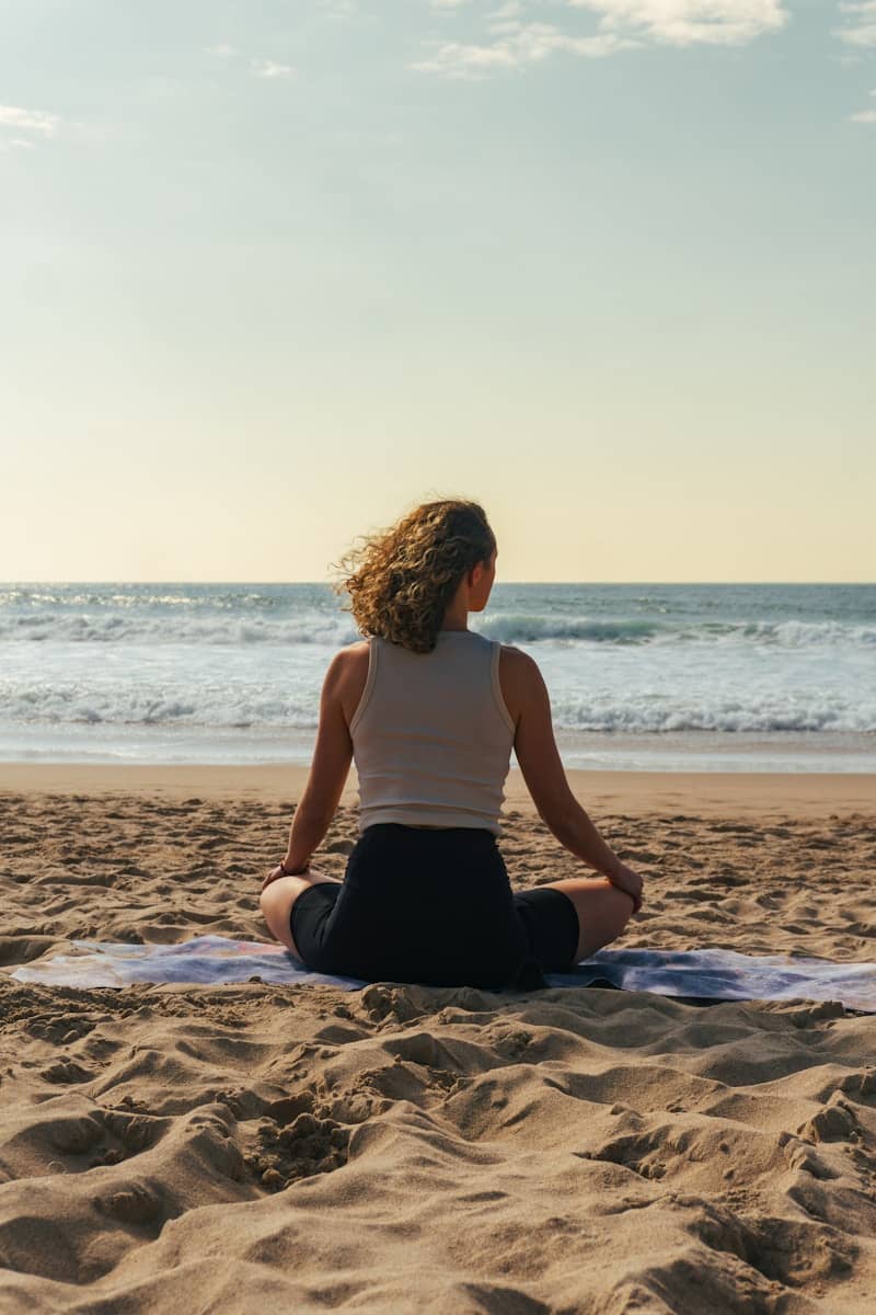 Woman meditating on a beach mat by the ocean.