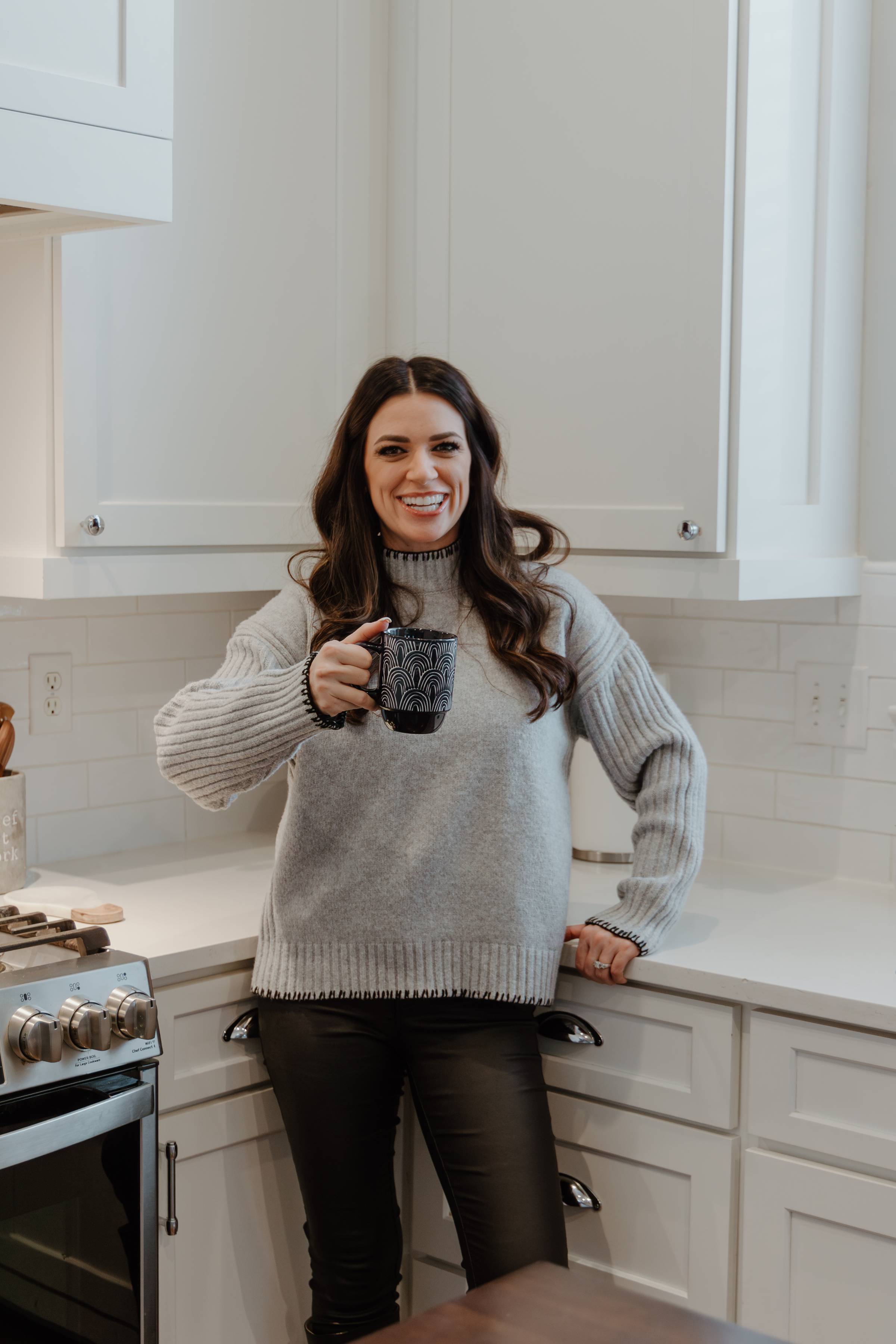 Carrissa Hickey of Lavish Interiors standing in a bright, modern kitchen holding a mug, welcoming readers to the first edition of The Lavish Letter.