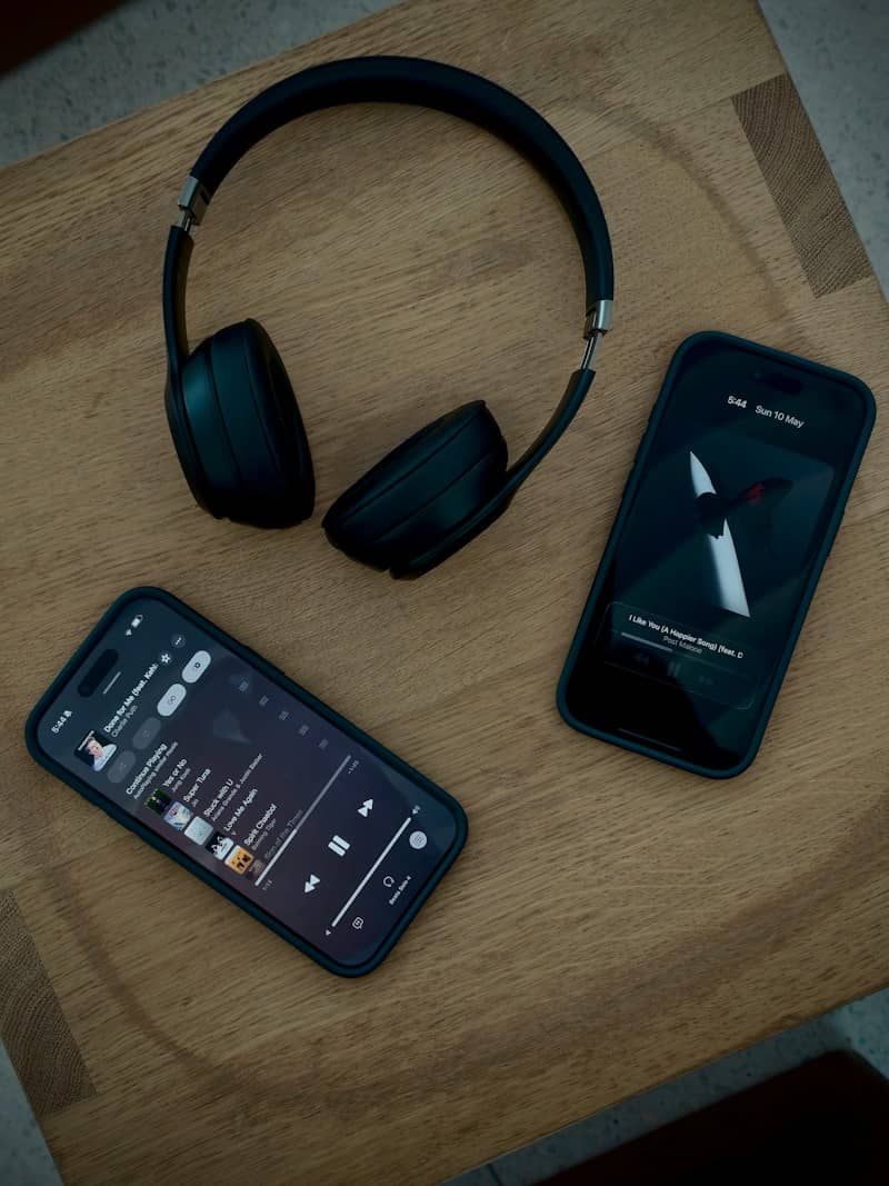 Two smartphones and black headphones on a wooden surface