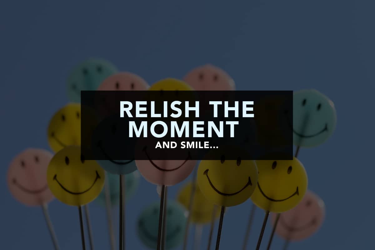 A collection of multi-coloured smiley faces on sticks. Over the top of this 'bouquet' is bold pale blue text that reads "Relish the moment and smile..."