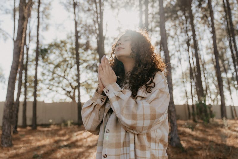 a woman standing in a forest praying