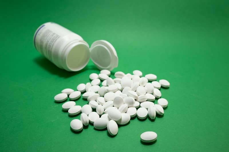 White pills spilled from an open bottle on green background