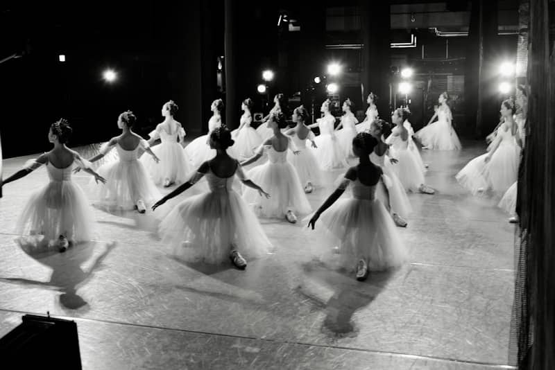 Dancers in white tutus practice on a stage