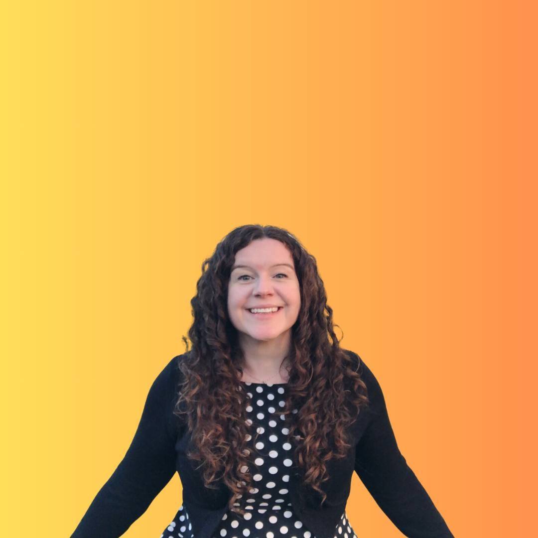 Sam is smiling at the camera wearing a black and white polka dot dress and a black cardigan. Behind her is a gradient yellow and orange background, like a sunrise